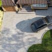 Aerial view of a modern residential driveway paved with Brett Alpha 50mm block paving in Silver Haze. The driveway features a neat curved edge along a well-maintained lawn and a charcoal border, with a parked black SUV in front of a brick house with a tiled roof