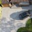 Aerial view of a modern residential driveway paved with Brett Alpha 50mm block paving in Silver Haze. The driveway features a neat curved edge along a well-maintained lawn and a charcoal border, with a parked black SUV in front of a brick house with a tiled roof